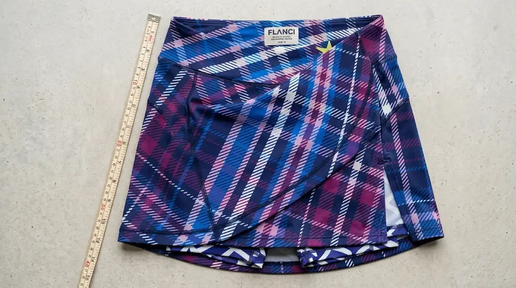 Flat lay of a plaid FLANCI skort laid next to a measuring stick for fit and fabric technical specifications.
