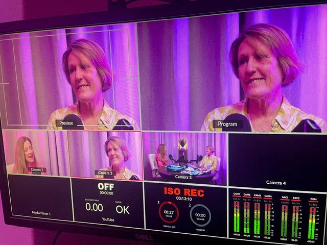 Video production screen showing multi-camera setup with two women in studio interview under purple lighting